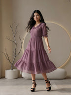 Woman wearing a mauve tiered dress with ruffled details in a modern living room setting