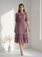Woman wearing a mauve tiered midi dress with ruffled details in a minimalist bright room