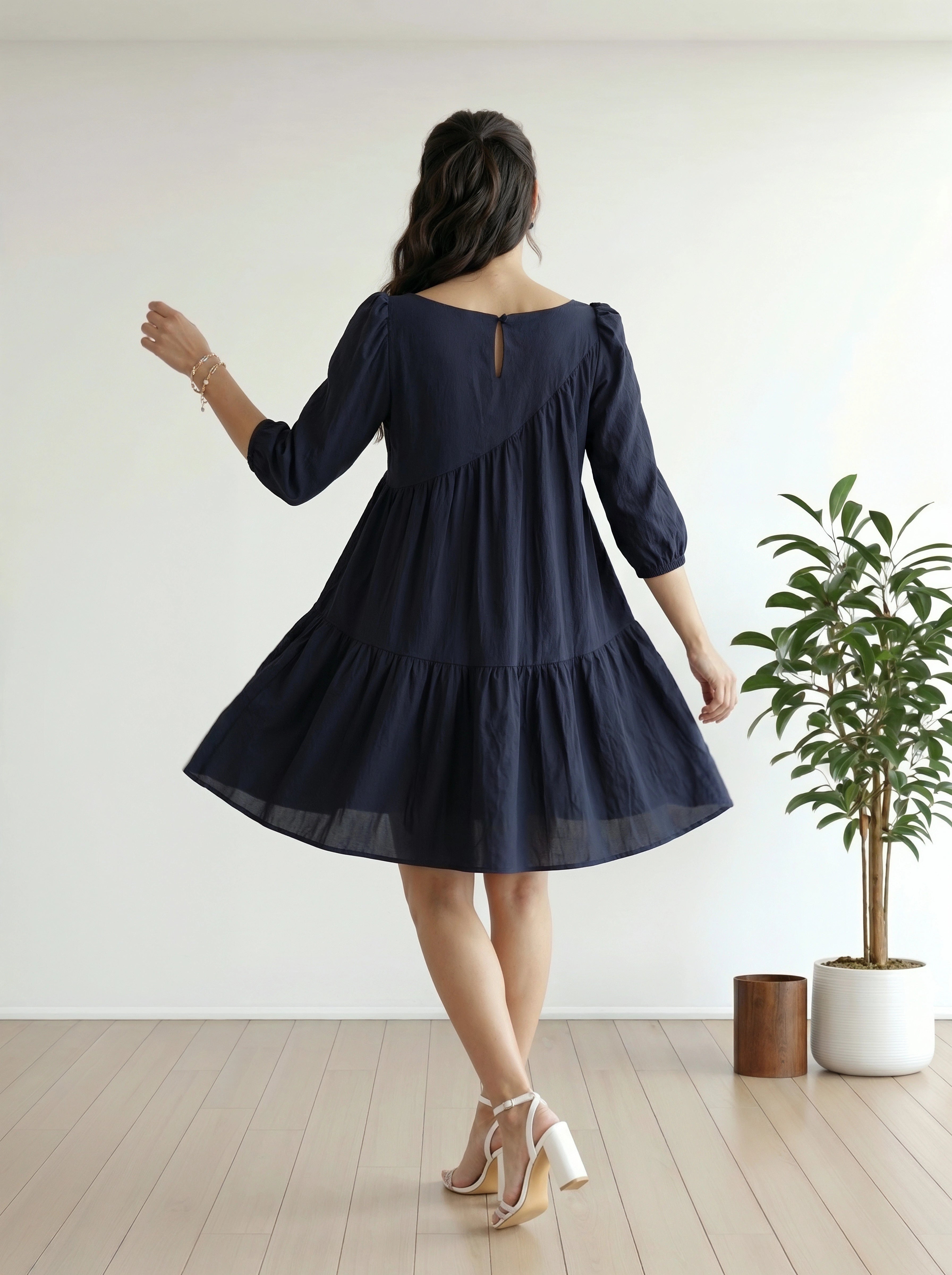 Woman wearing a navy blue dress in a minimalistic room with a plant.