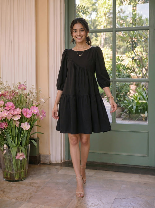 Woman in a black dress standing in a room with flowers and a green door.