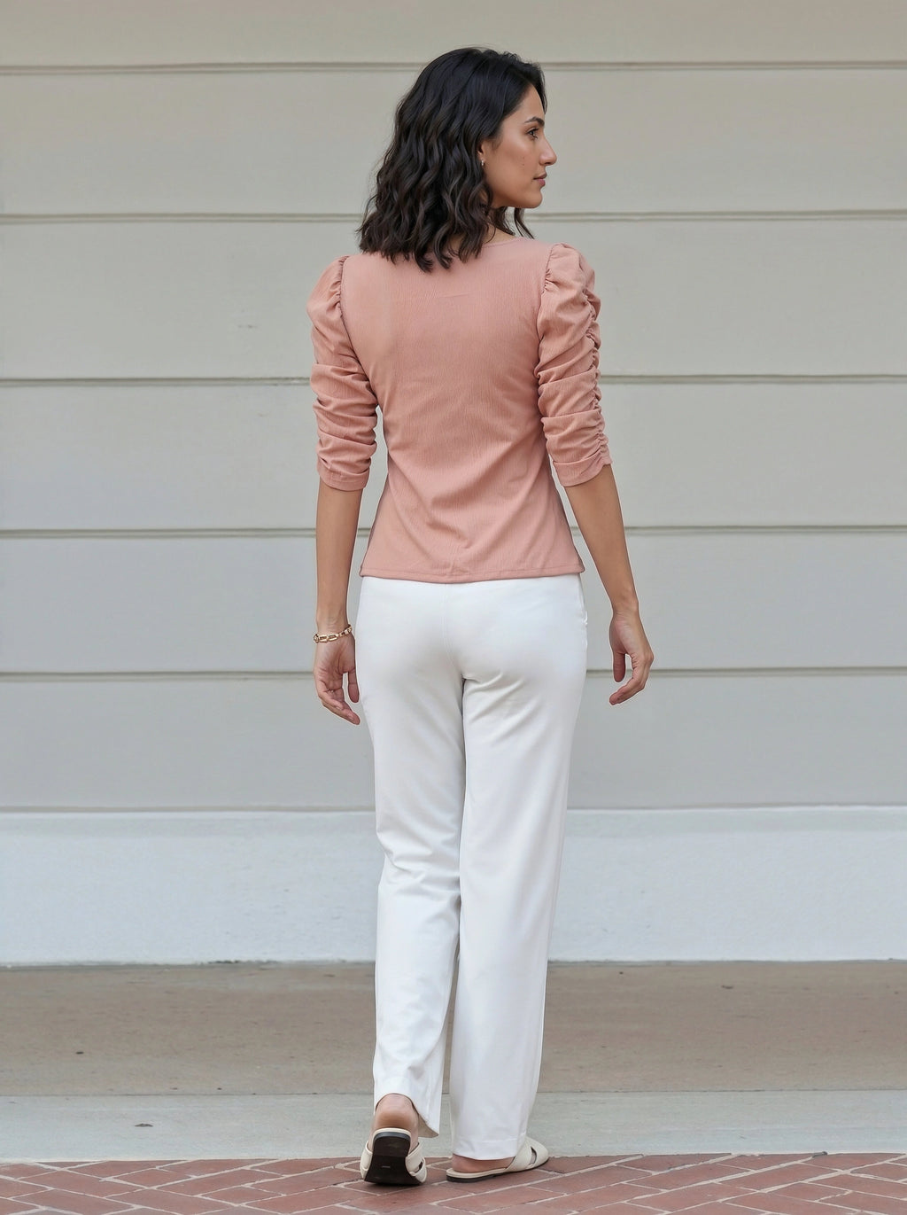 Woman wearing a pink top and white pants standing on a porch.
