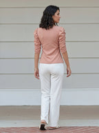 Woman wearing a pink top and white pants standing on a porch.