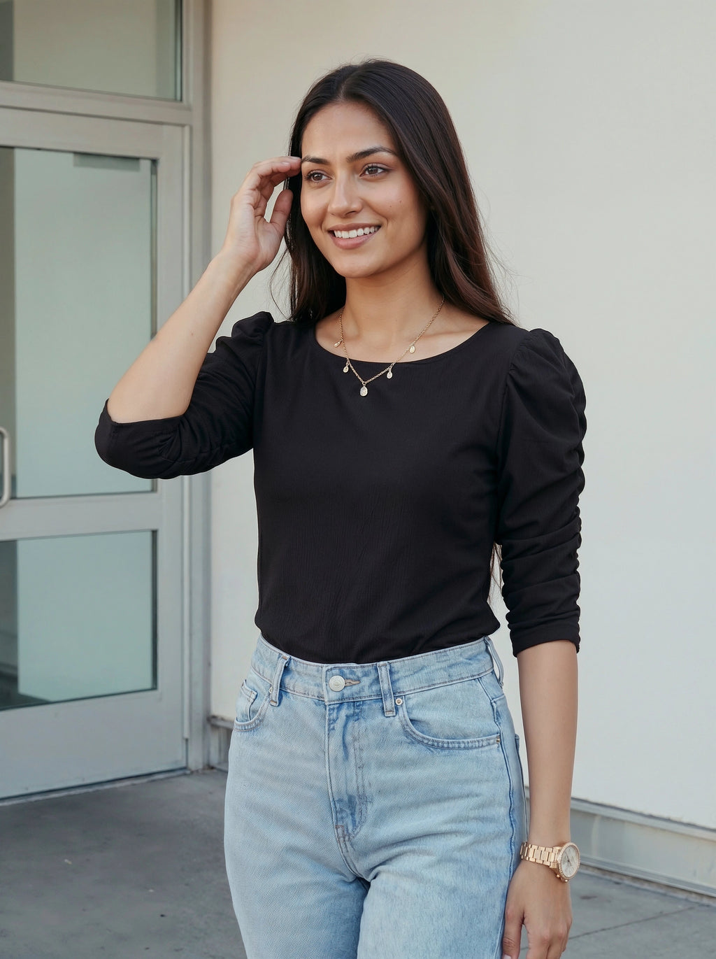 Woman wearing a black top and light blue jeans standing outdoors.