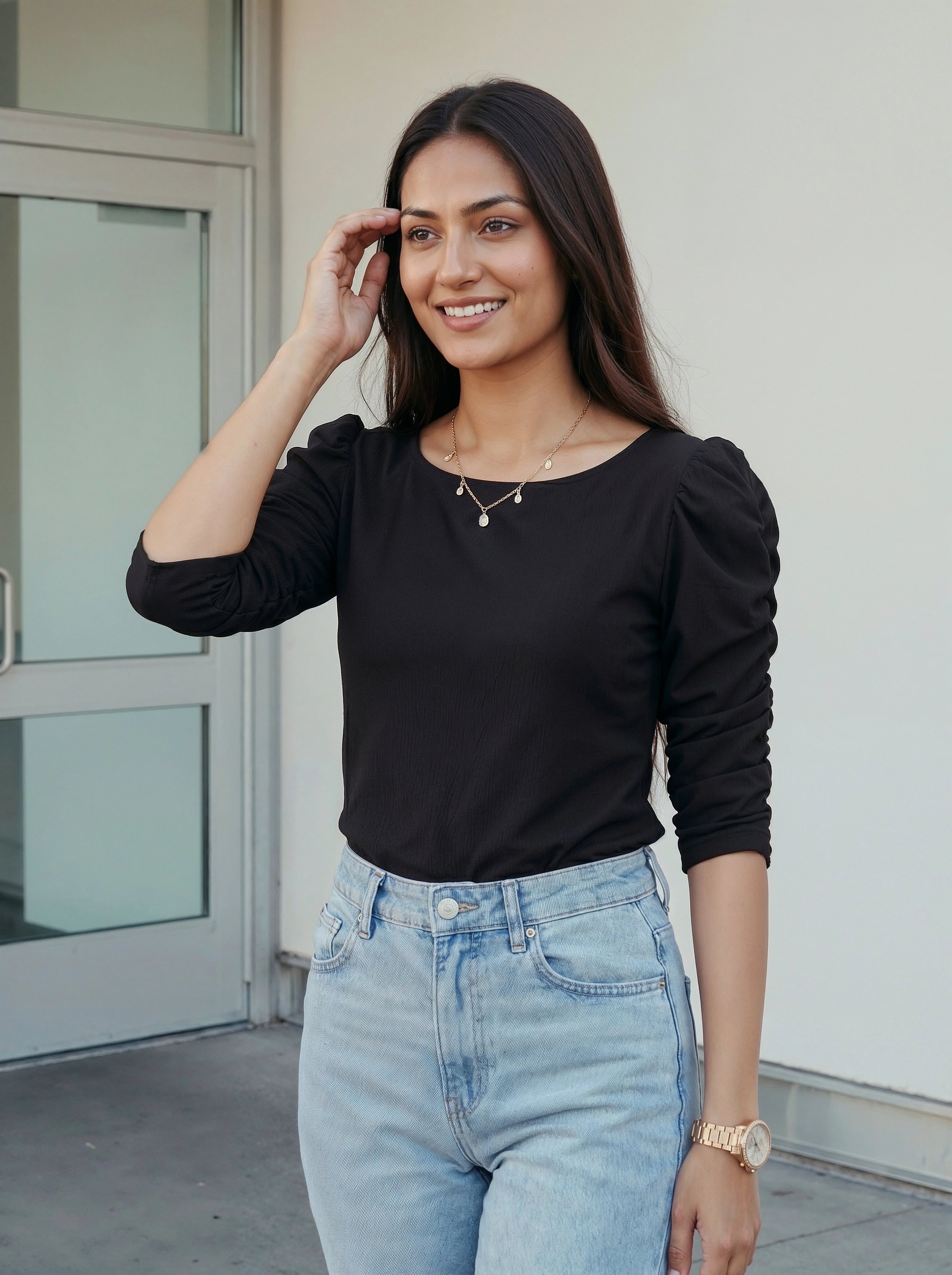 Woman wearing a black top and light blue jeans standing outdoors.