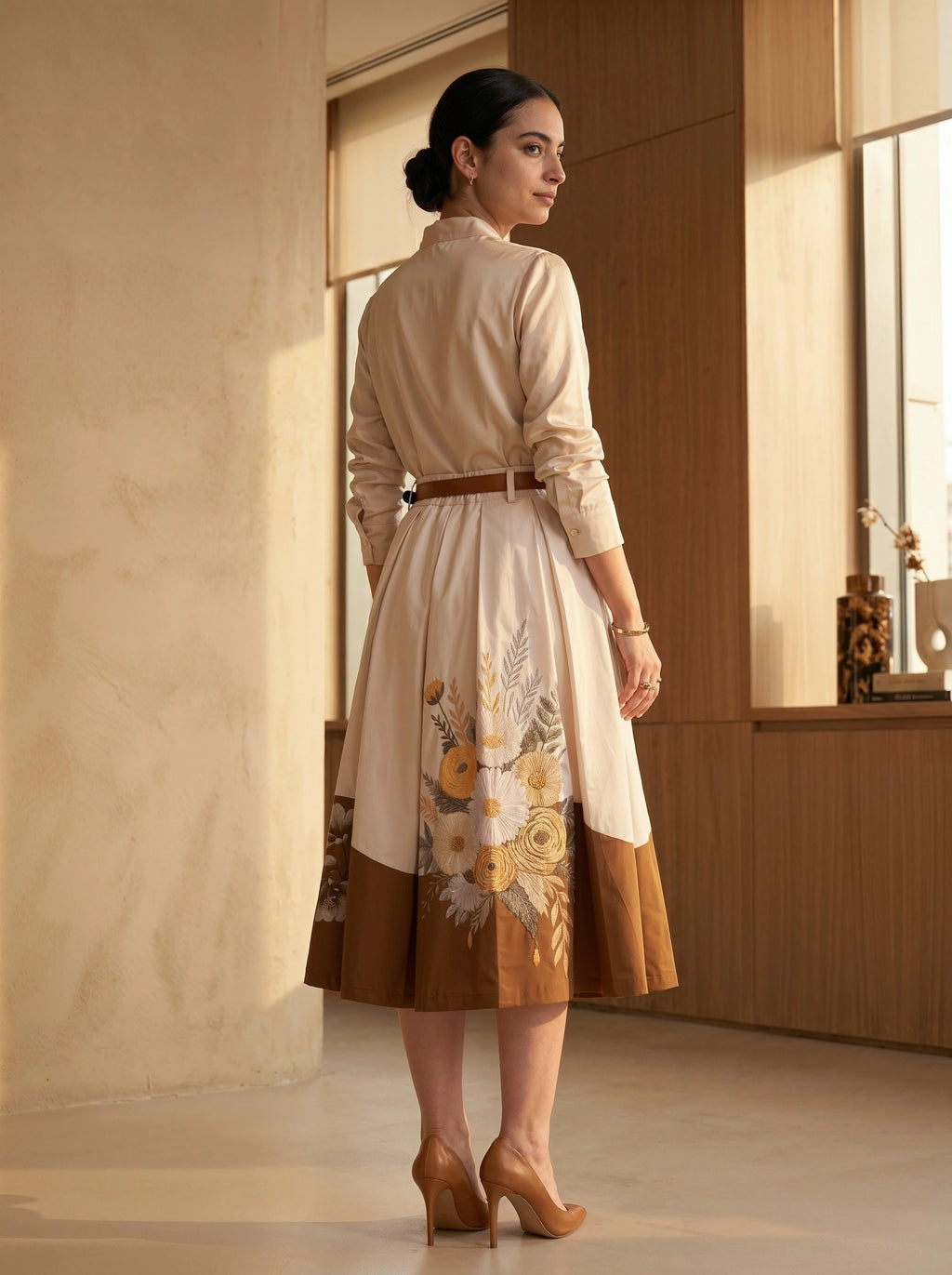 Woman wearing a beige dress with floral patterns in a room with wooden paneling.
