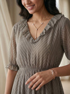 Woman wearing a gray dress with a subtle pattern, smiling and looking to the side.