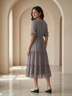Woman in a gray dress standing in an archway with soft lighting
