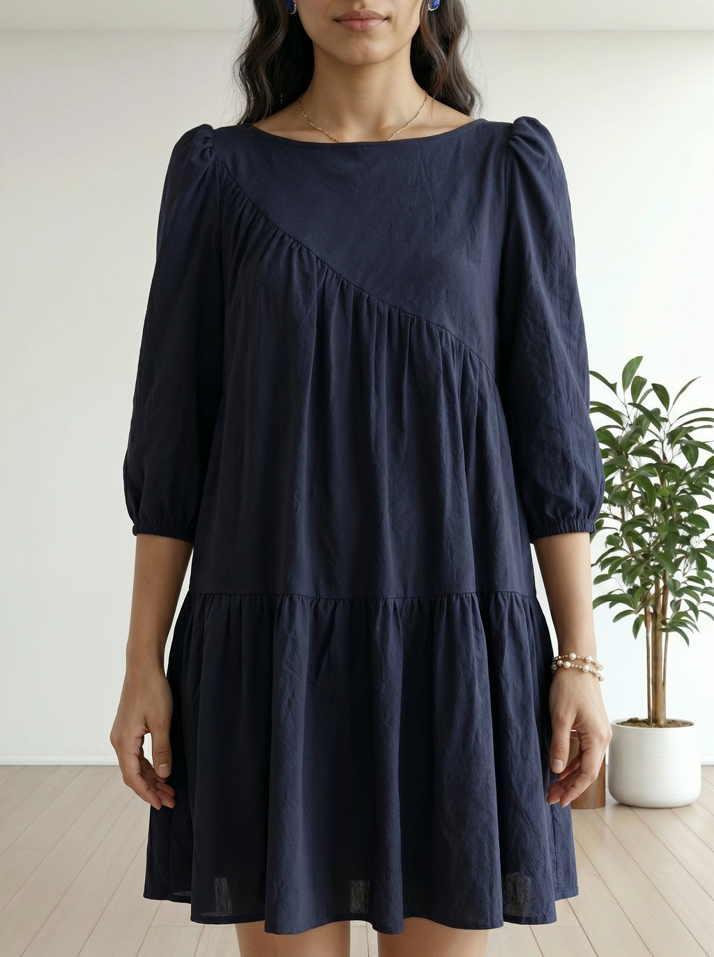 Woman wearing a navy blue dress with puffed sleeves in a minimal indoor setting.