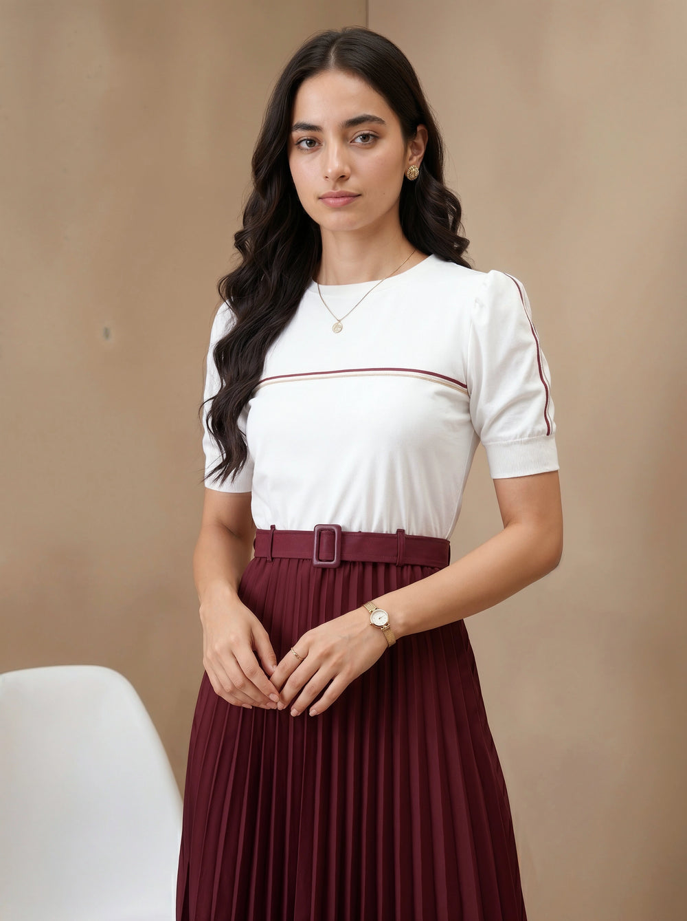 Woman wearing a white top with red trim and a maroon pleated skirt against a beige background