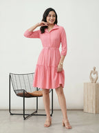 Woman wearing a pink dress standing in a minimalistic room with a chair and sculpture.