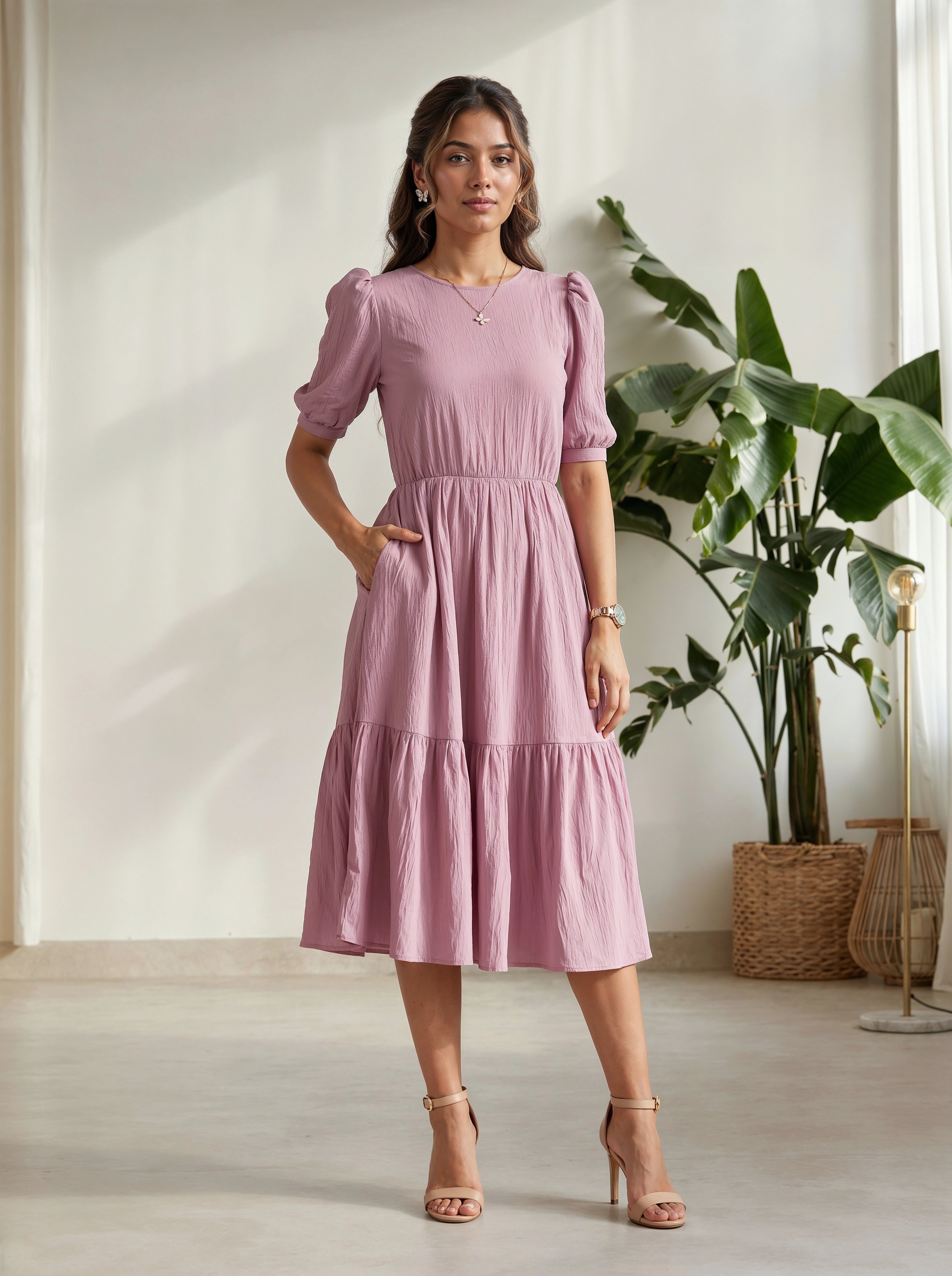Woman wearing a pink dress standing in a room with a plant and light-colored floor.