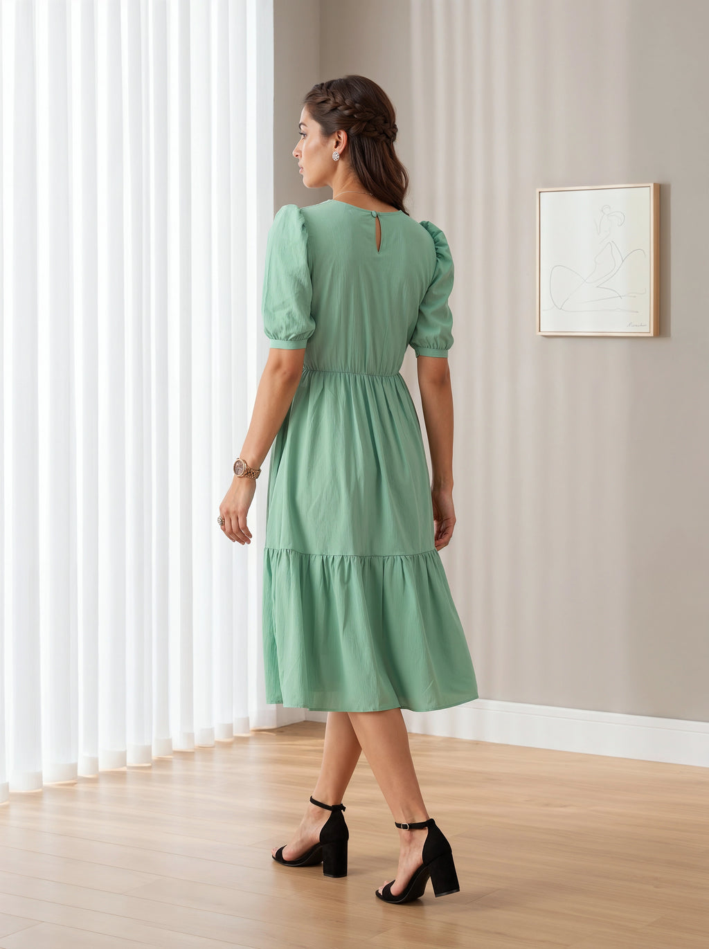 Woman wearing a green dress standing in a room with light-colored walls and wooden floor.