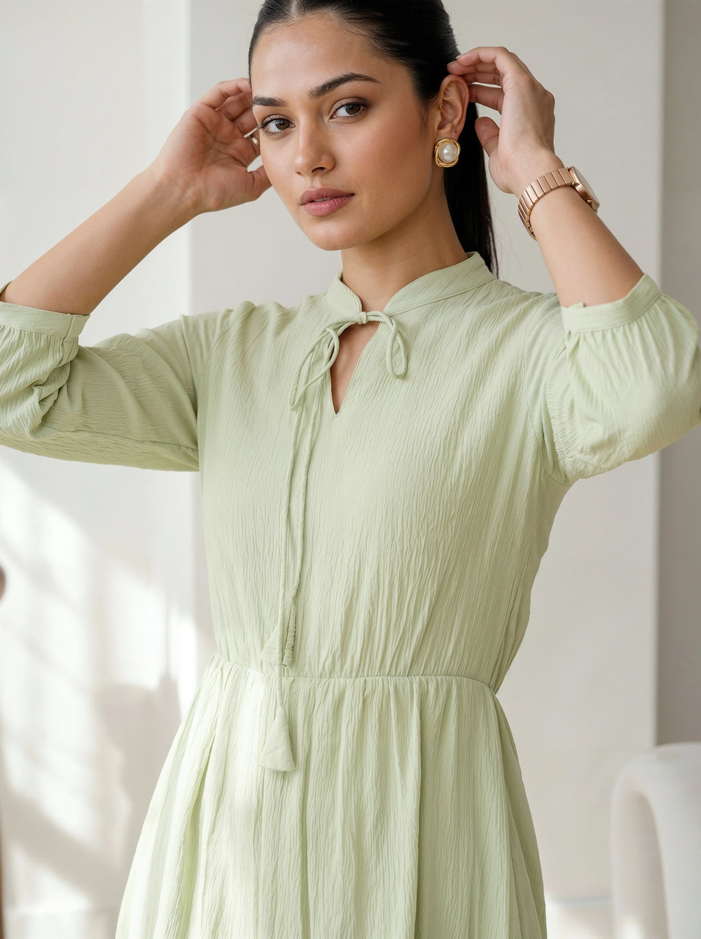 Woman wearing a light green dress with pearl earrings indoors