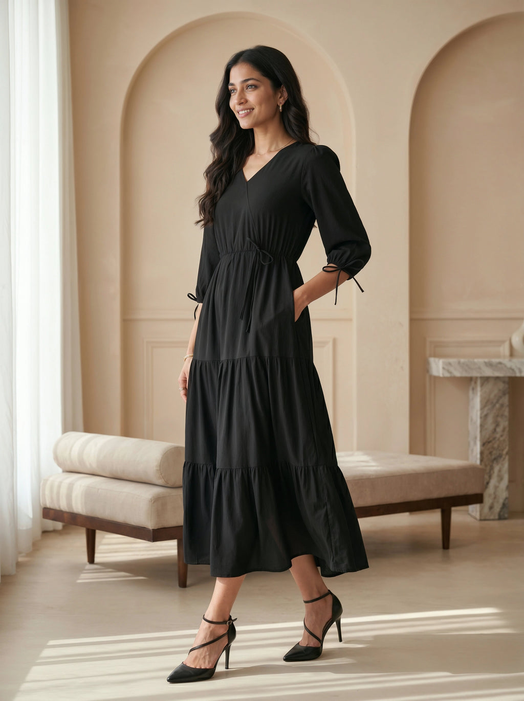 Woman wearing a black dress standing in an elegant room with arched doorways.