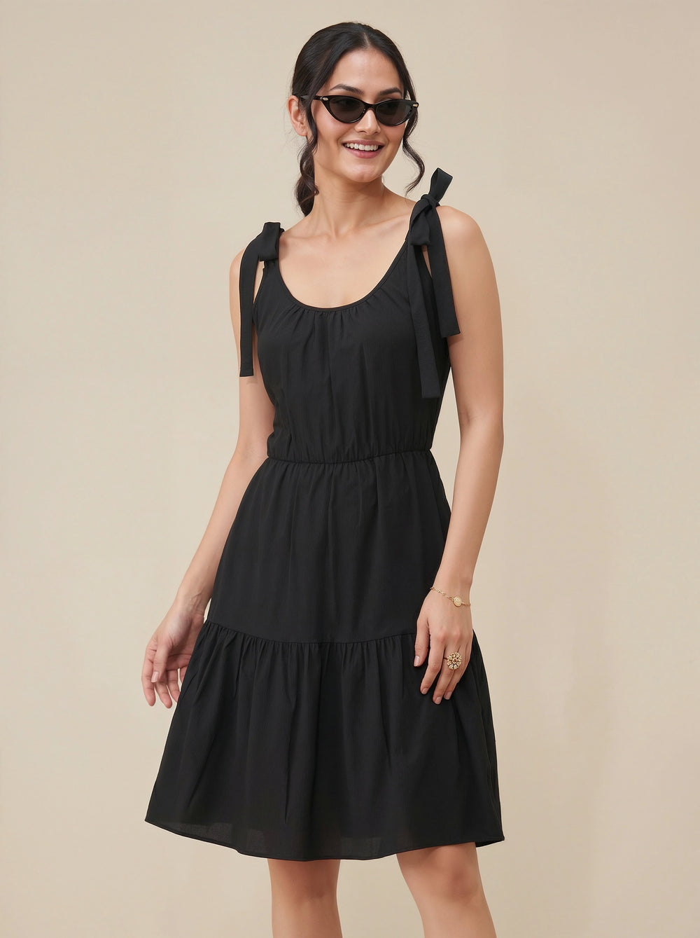 Woman wearing a black dress with bow straps on a beige background