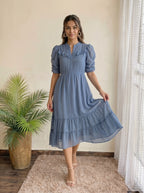Woman smiling in a tiered dusty blue dress in a bright room