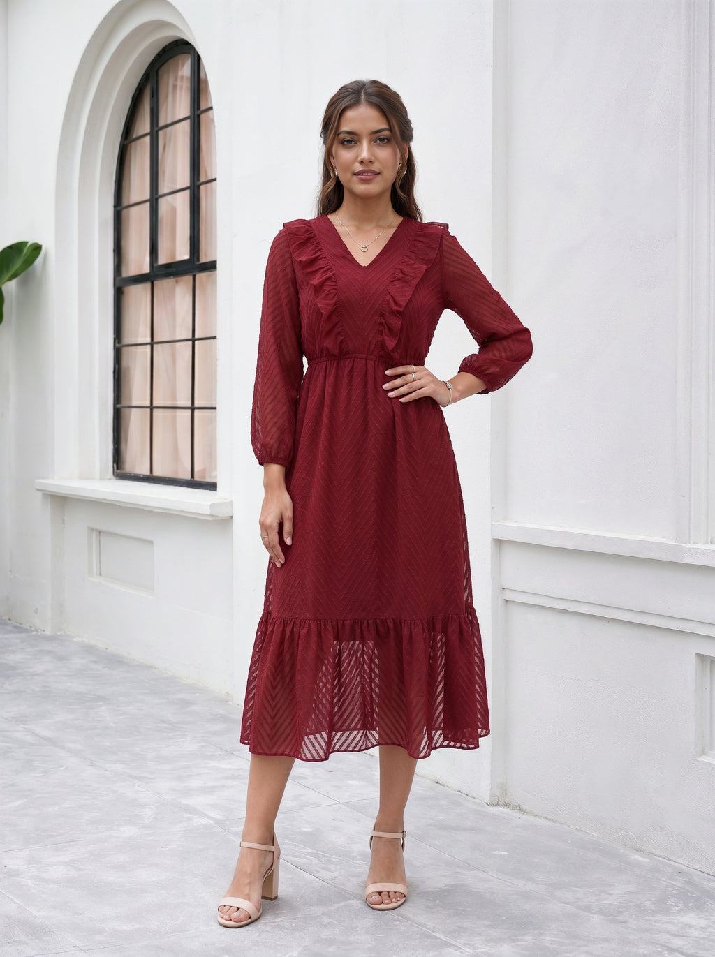 Woman wearing a burgundy dress standing in front of a white wall with an arched window.