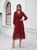 Woman wearing a burgundy dress standing in front of a white wall with an arched window.