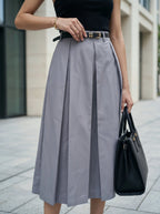 Person wearing a gray skirt and black top, holding a black handbag on a city street.