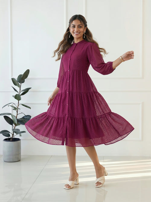Woman wearing a burgundy dress standing in a bright room with a plant in the background