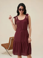 Woman wearing a burgundy dress with bow straps against a beige background