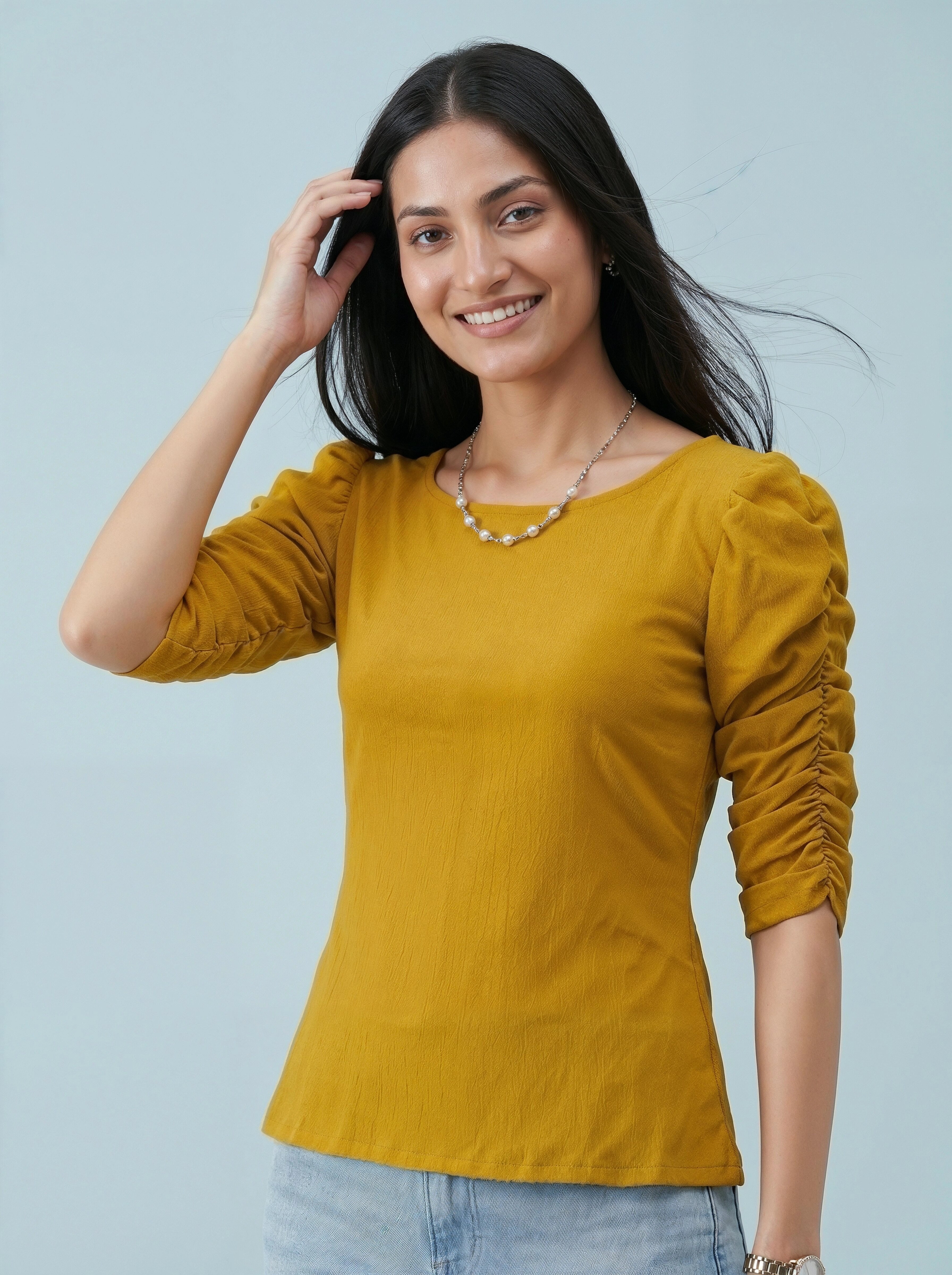 Woman wearing a yellow top with ruched sleeves against a light blue background