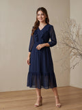 Woman wearing a navy blue dress standing against a beige wall.