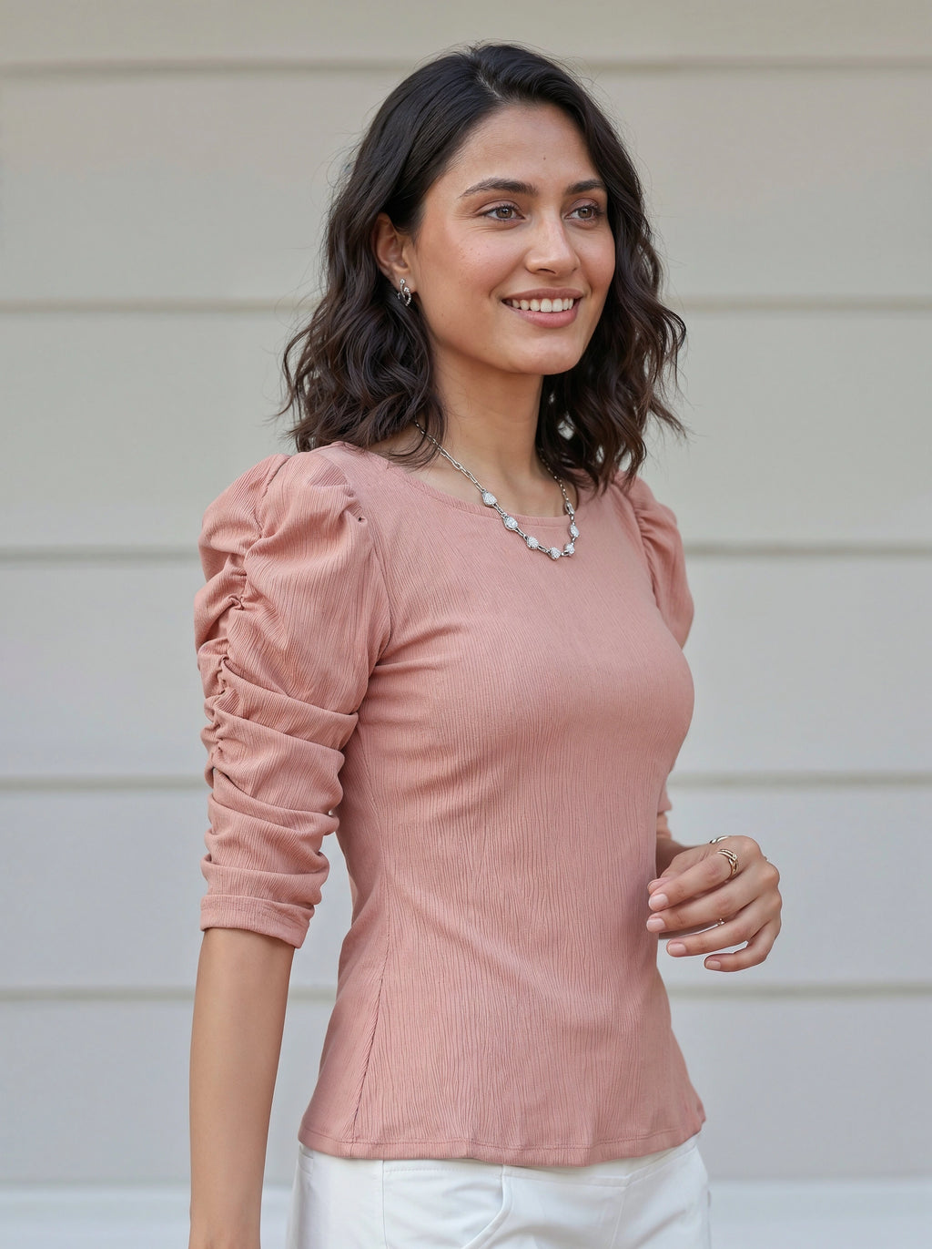 Woman wearing a pink long-sleeve top with ruched sleeves against a neutral background