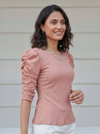 Woman wearing a pink long-sleeve top with ruched sleeves against a neutral background