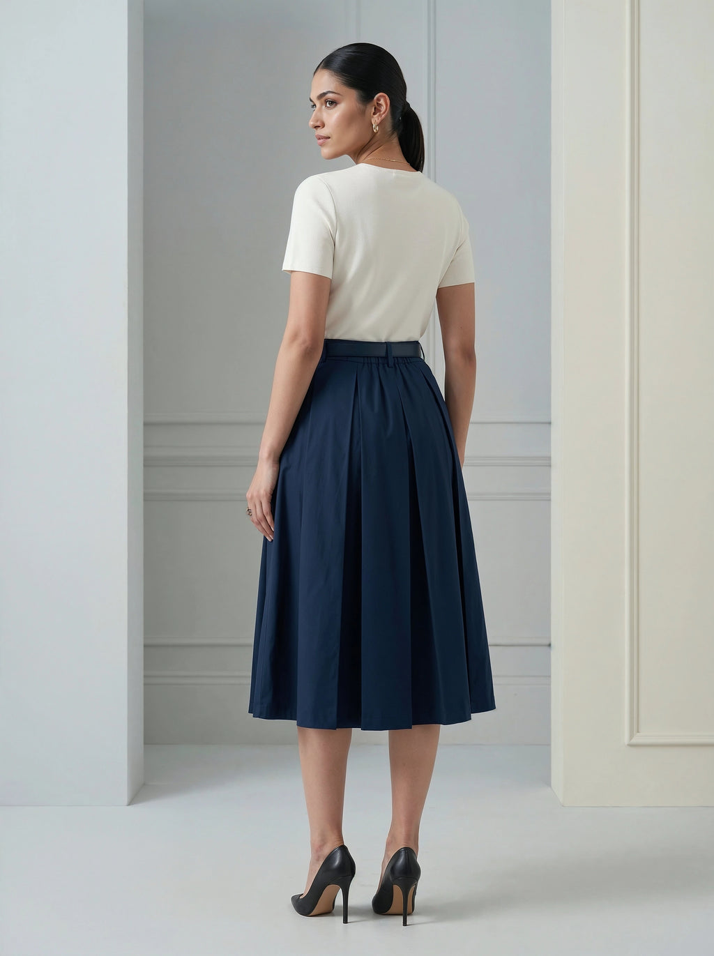 Woman wearing a white top and navy skirt in a minimalistic setting