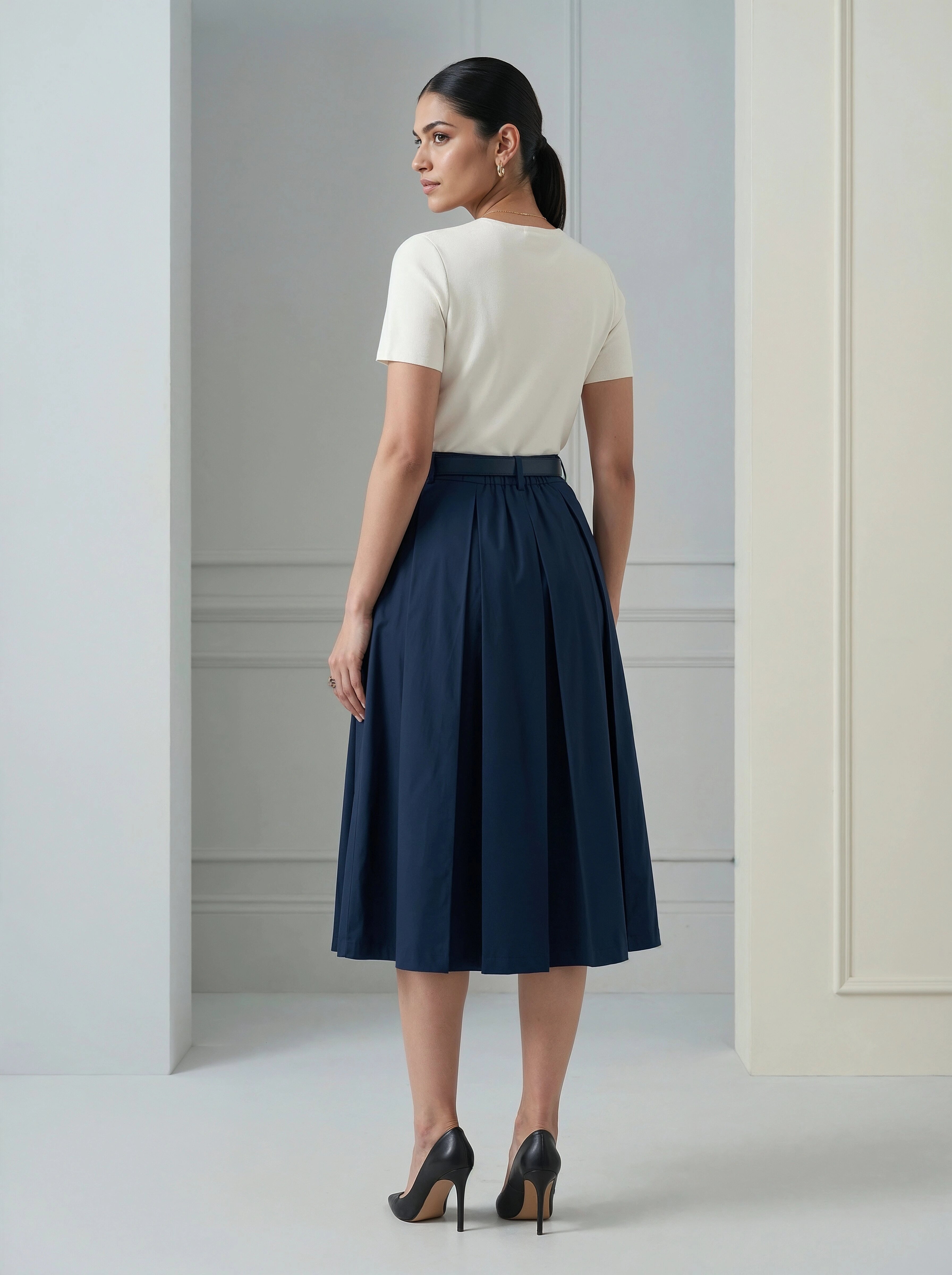 Woman wearing a white top and navy skirt in a minimalistic setting