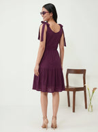 Woman wearing a purple dress with bow straps, standing against a white background.