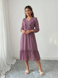 Woman wearing a purple dress standing against a white wall.