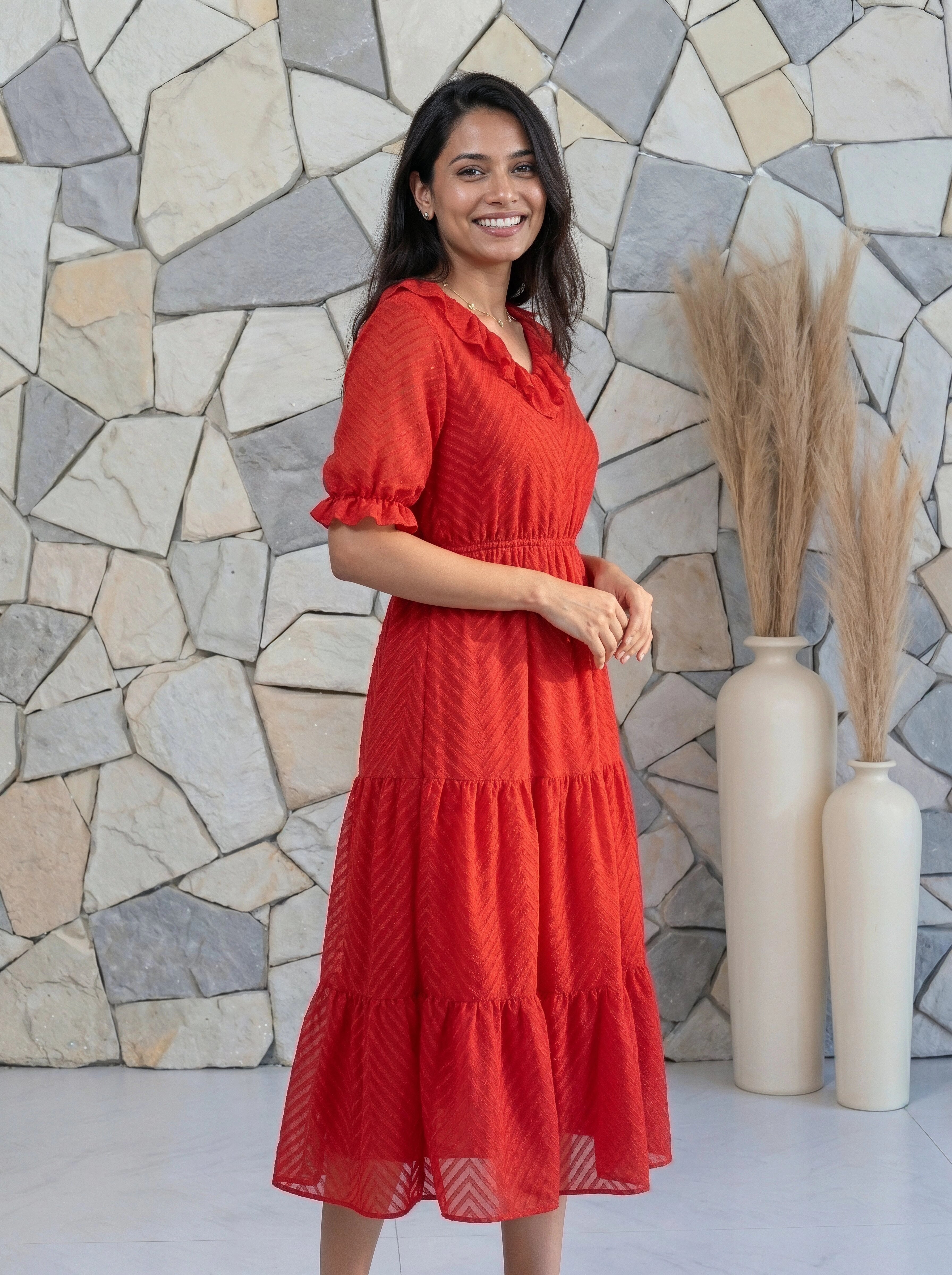 Woman in a red dress standing against a stone wall with decorative vases.