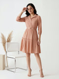 Woman wearing a peach-colored dress standing in a minimalistic room with a chair and decorative elements.