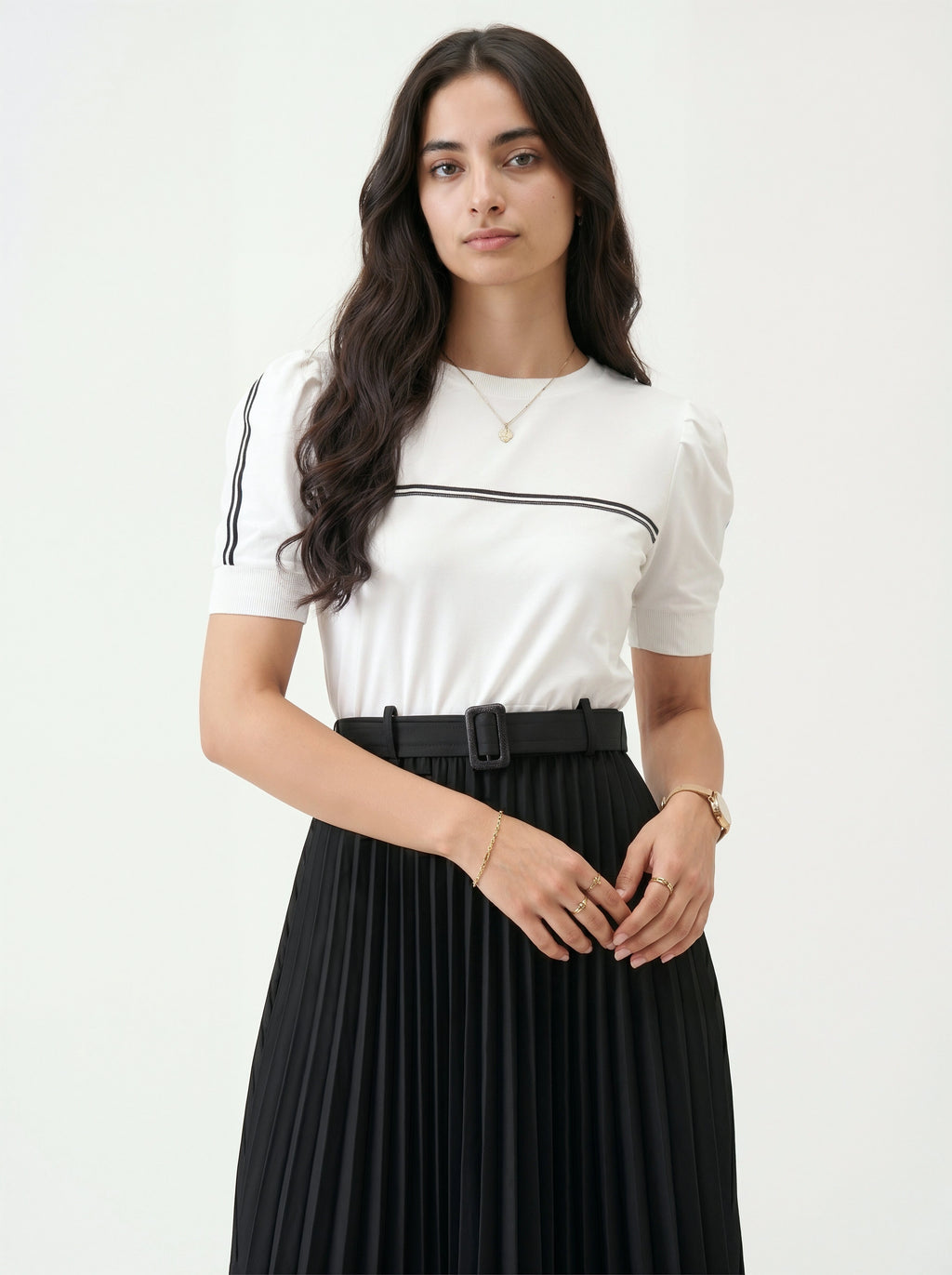 Woman wearing a white top with black trim and a black pleated skirt on a white background