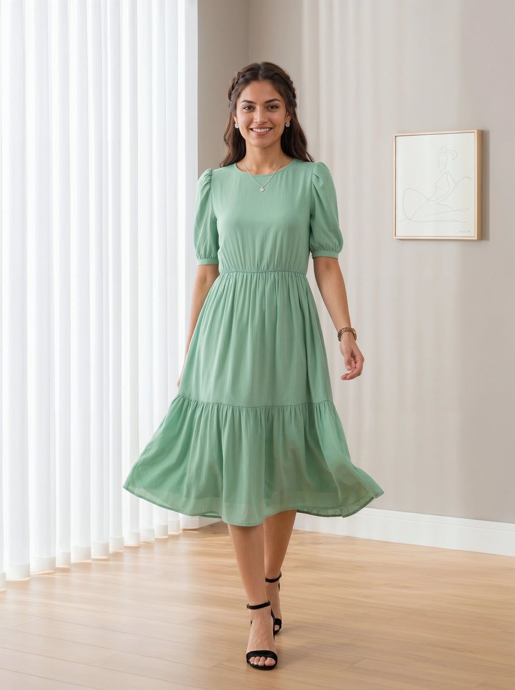 Woman wearing a green dress standing in a room with light-colored walls and wooden floor.