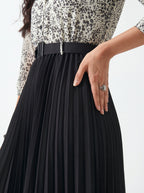 Person wearing a black pleated skirt with a patterned top on a white background