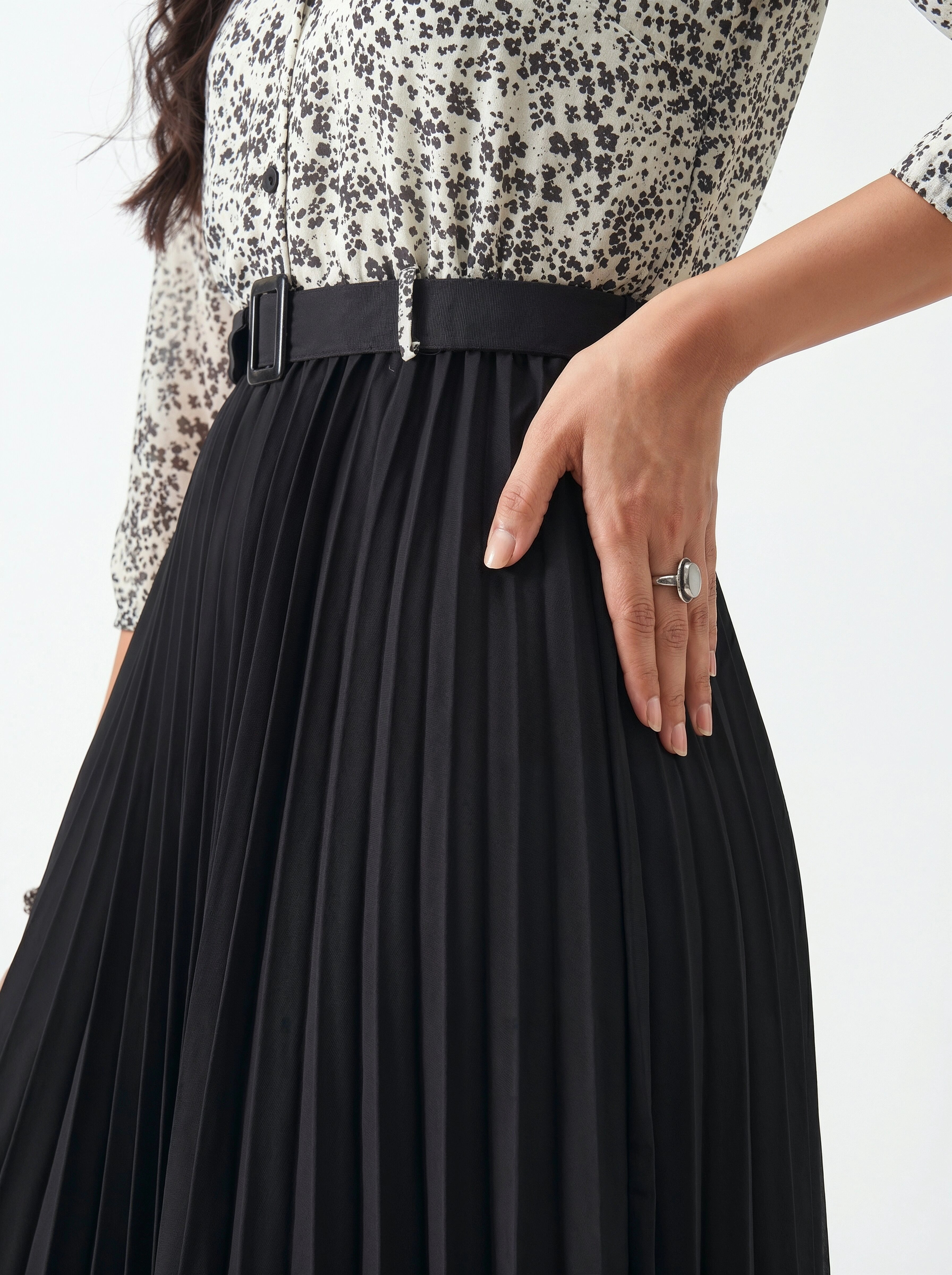 Person wearing a black pleated skirt with a patterned top on a white background