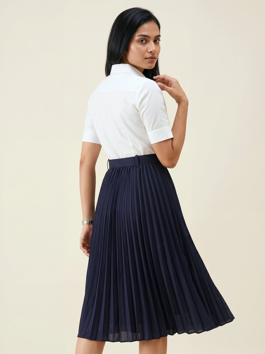 Woman wearing a white shirt and navy pleated skirt on a beige background
