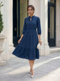 Woman wearing a blue dress standing in front of a building entrance.