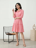 Woman wearing a pink dress standing in a minimalistic room with a chair and sculpture.