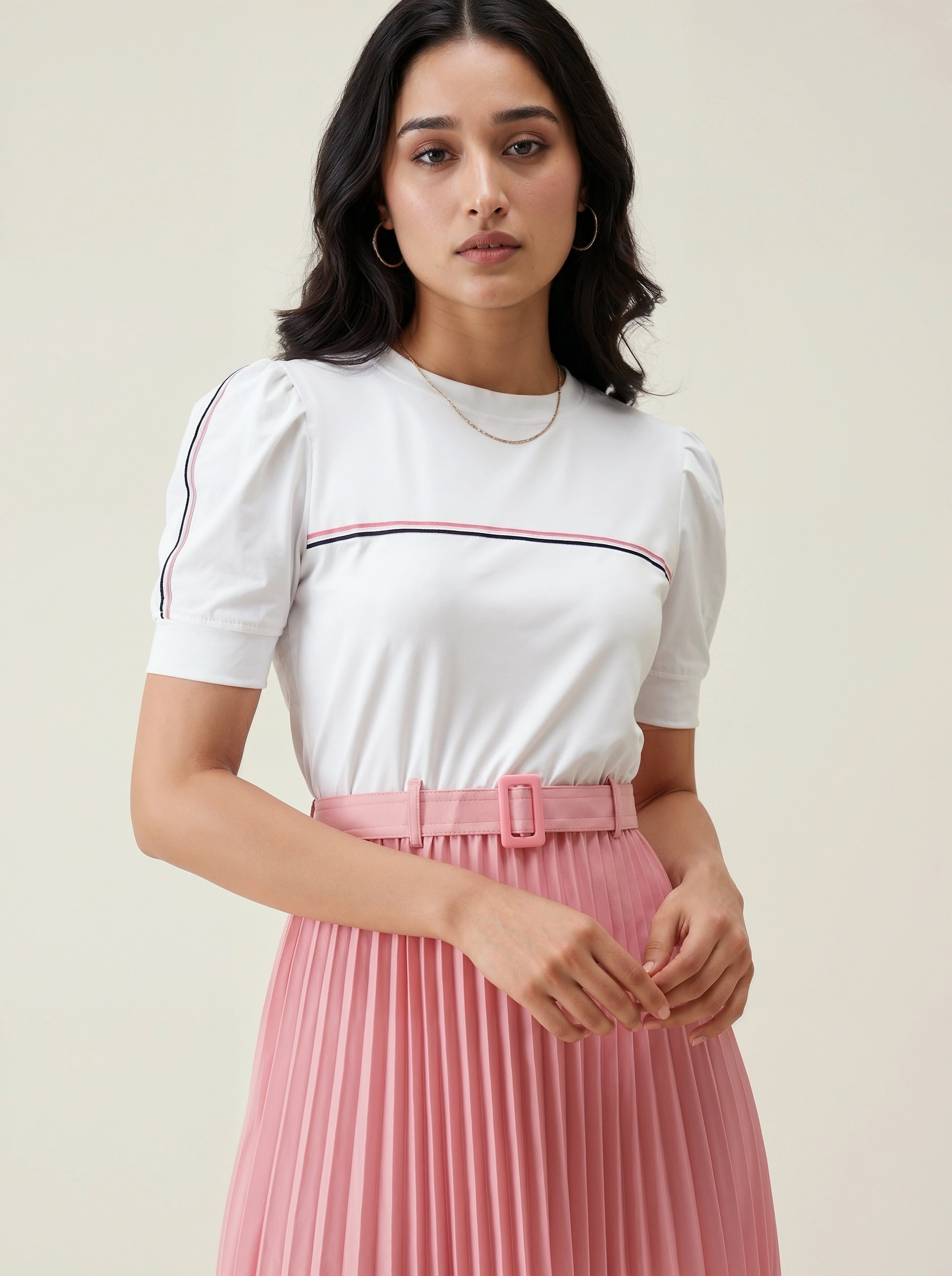 Woman wearing a white top with a red and blue stripe and a pink pleated skirt on a beige background
