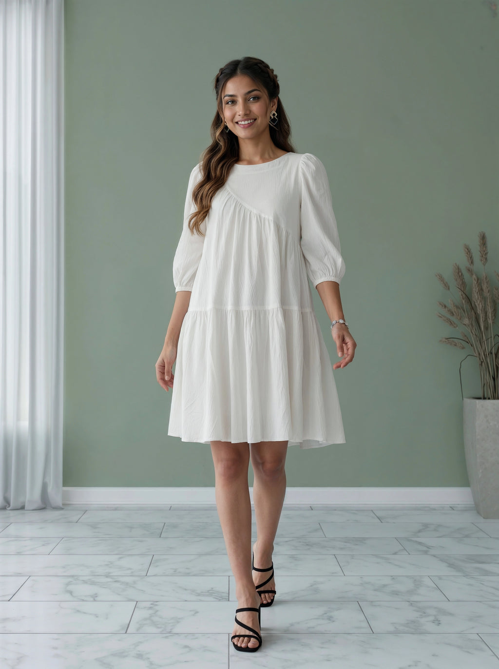 Woman wearing a white dress standing in a room with a green wall and a plant.