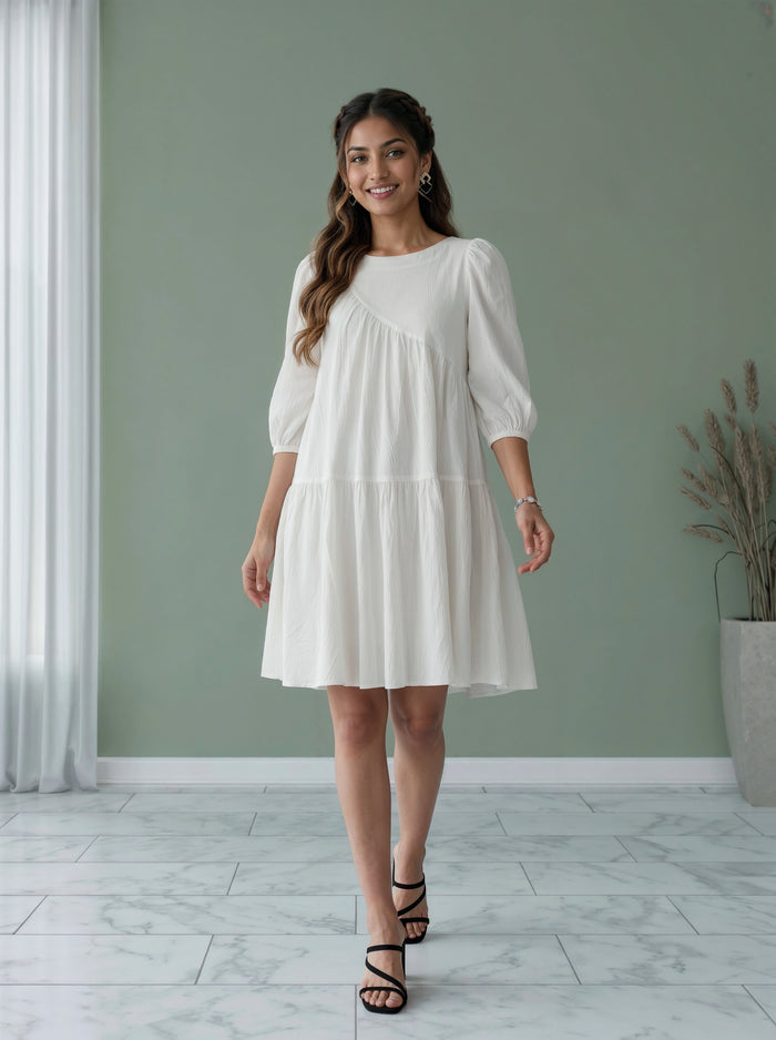 Woman wearing a white dress standing in a room with a green wall and a plant.