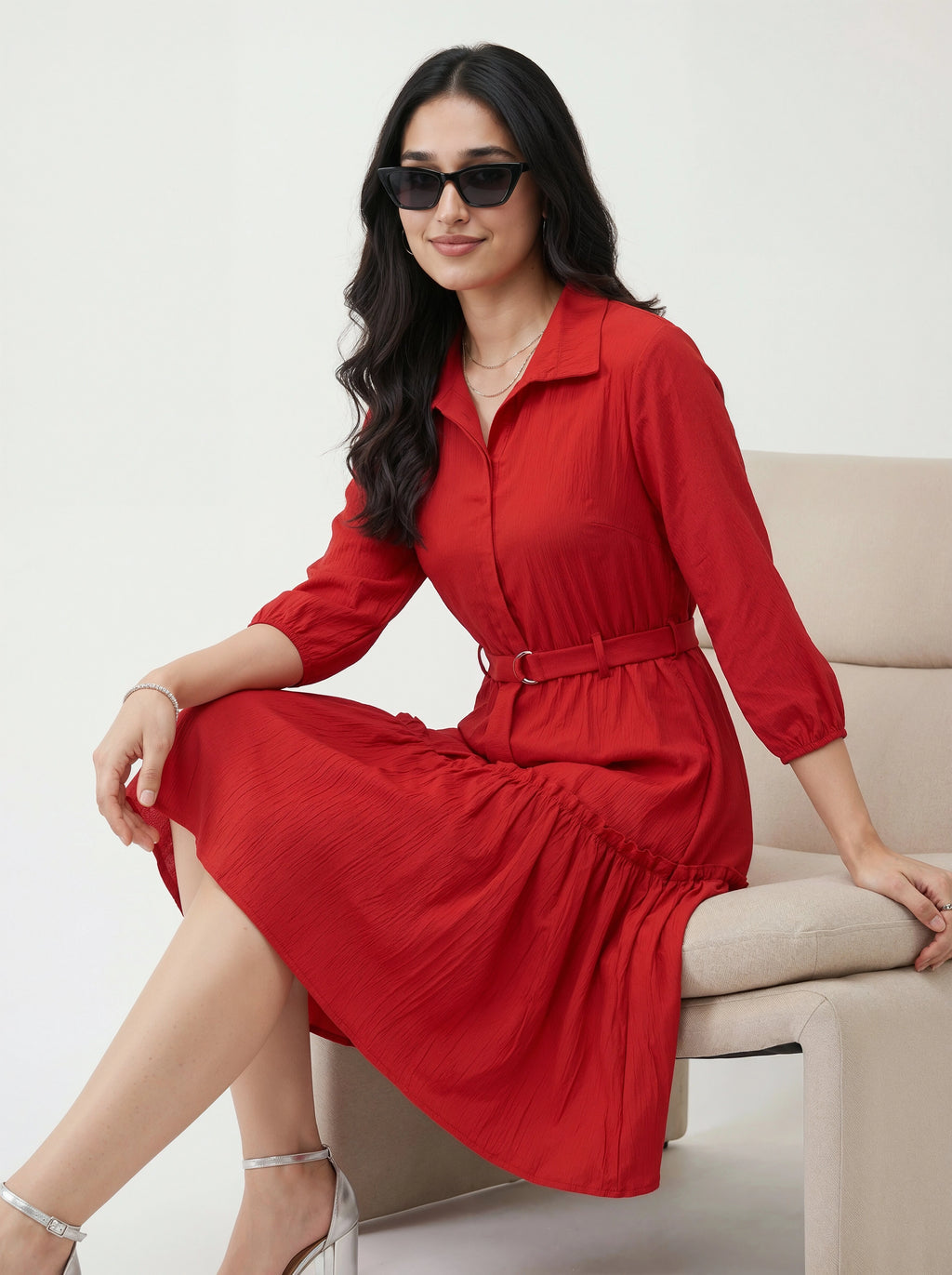 Woman in a red dress sitting on a beige chair against a white background