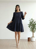 Woman wearing a navy blue dress standing in a minimalistic room with a plant.