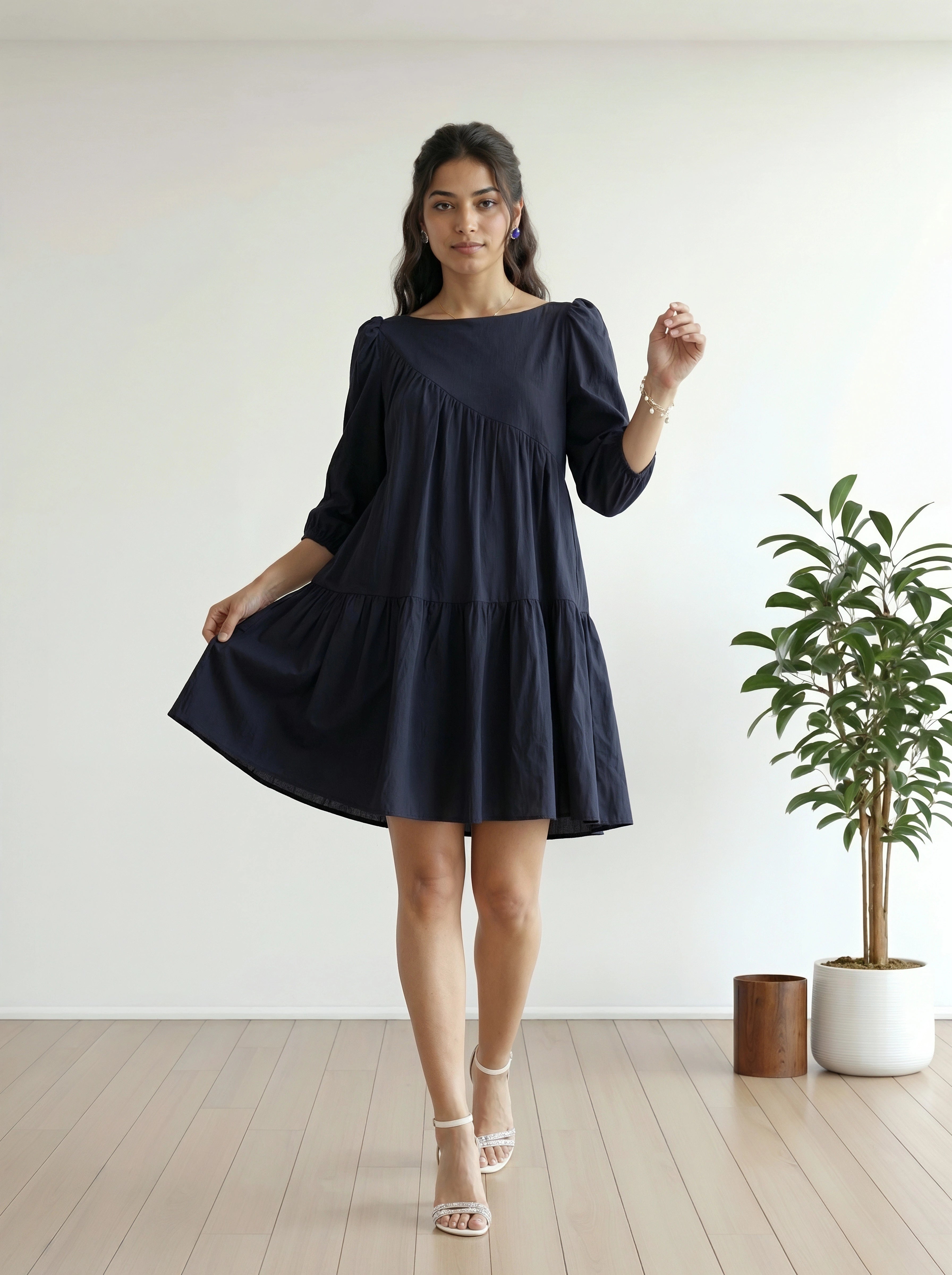 Woman wearing a navy blue dress standing in a minimalistic room with a plant.