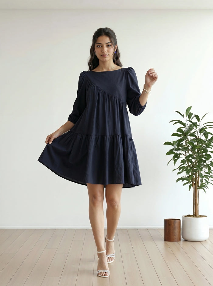 Woman wearing a navy blue dress standing in a minimalistic room with a plant.