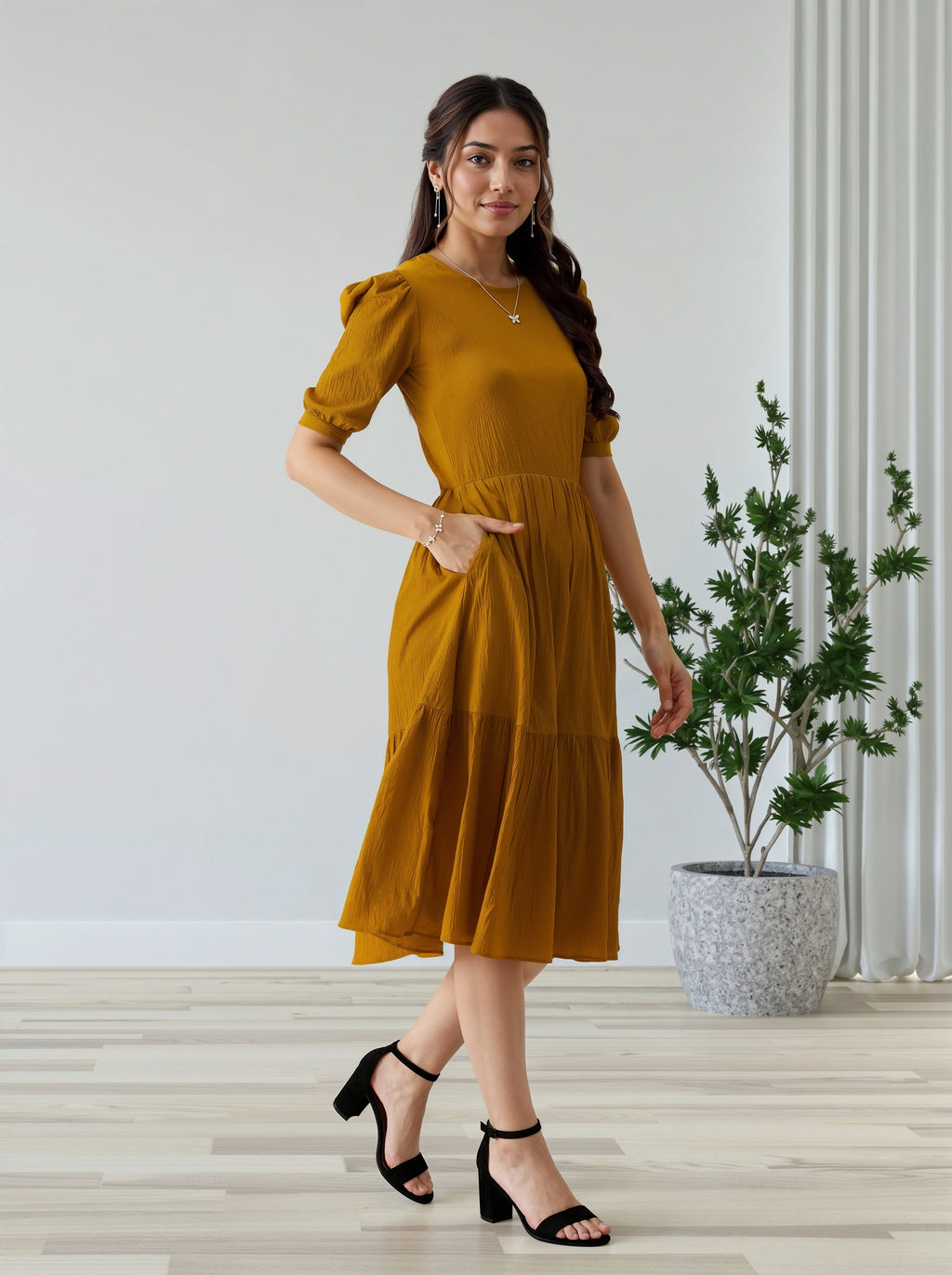 Woman in a mustard yellow dress standing indoors with a plant in the background